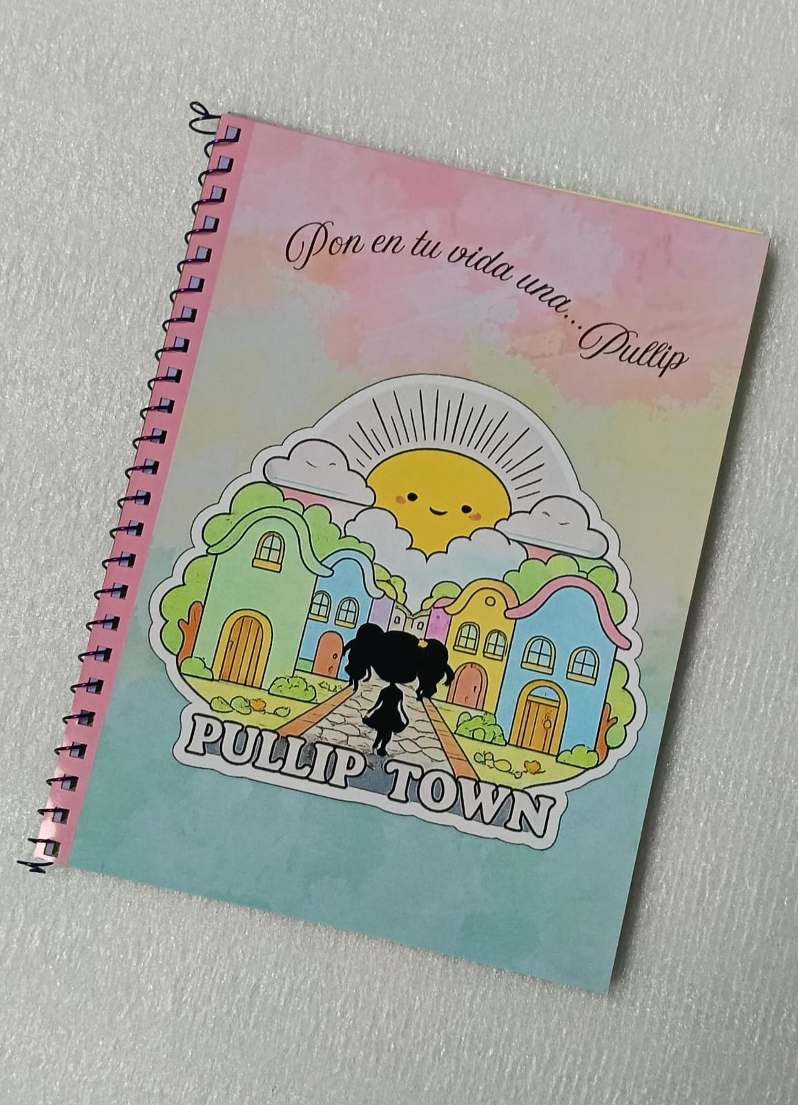 Libreta Oficial de Pullip Town Barcelona 2026 Guarda tus ideas, bocetos, recuerdos y momentos especiales en la Libreta Oficial de Pullip Town Barcelona 2026, una pieza de merchandising elaborada artesanalmente para conmemorar una edición muy especial del evento. Cada libreta está realizada a mano, lo que la convierte en un recuerdo único para coleccionistas y amantes del universo Pullip. Su interior está compuesto por páginas de colores, ideales para escribir, dibujar, pegar fotografías o conservar autógrafos y recuerdos de tu visita al evento. Su práctico formato la hace perfecta para llevar contigo a convenciones, ferias o en tu día a día. Características Libreta oficial de Pullip Town Barcelona 2026. Elaborada completamente a mano. Páginas interiores de colores. Medidas: 20 × 15 cm. Producto de merchandising de edición especial. Información de entrega Este producto puede enviarse por correo. También puede recogerse en Pullip Town 2026 o en cualquiera de los eventos organizados por Dunia Eventos. Consulte los gastos de envío antes de realizar su pedido. Sobre el evento Pullip Town Barcelona 2026 se celebrará el 19 de septiembre de 2026 en el Hotel NH Collection Podium · Barcelona. Llévate un recuerdo artesanal de Pullip Town y conserva para siempre la magia de un evento pensado para todos los amantes de las muñecas Pullip